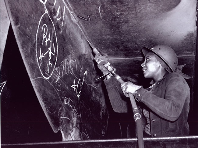 Black woman removing coatings and corrosion from ship