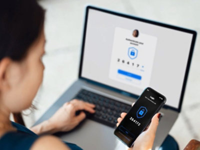 Žena pri prenosnom počítači, ktorá zadáva jednorazový prístupový kód vo svojom mobilnom telefóne pre bezpečné prihlásenie.