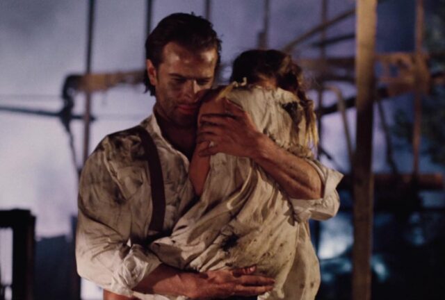 man in 1940s garb in a war zone carrying a little girl out of a bombed-out wreckage