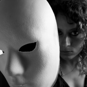 Young woman reveals her face behind white mask.