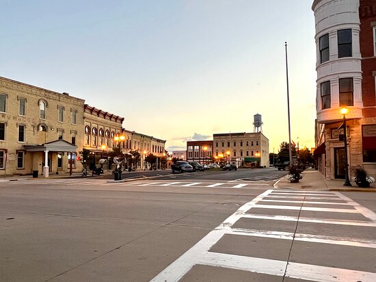 Downtown street at sunset with historic brick buildings and lit street lamps.
