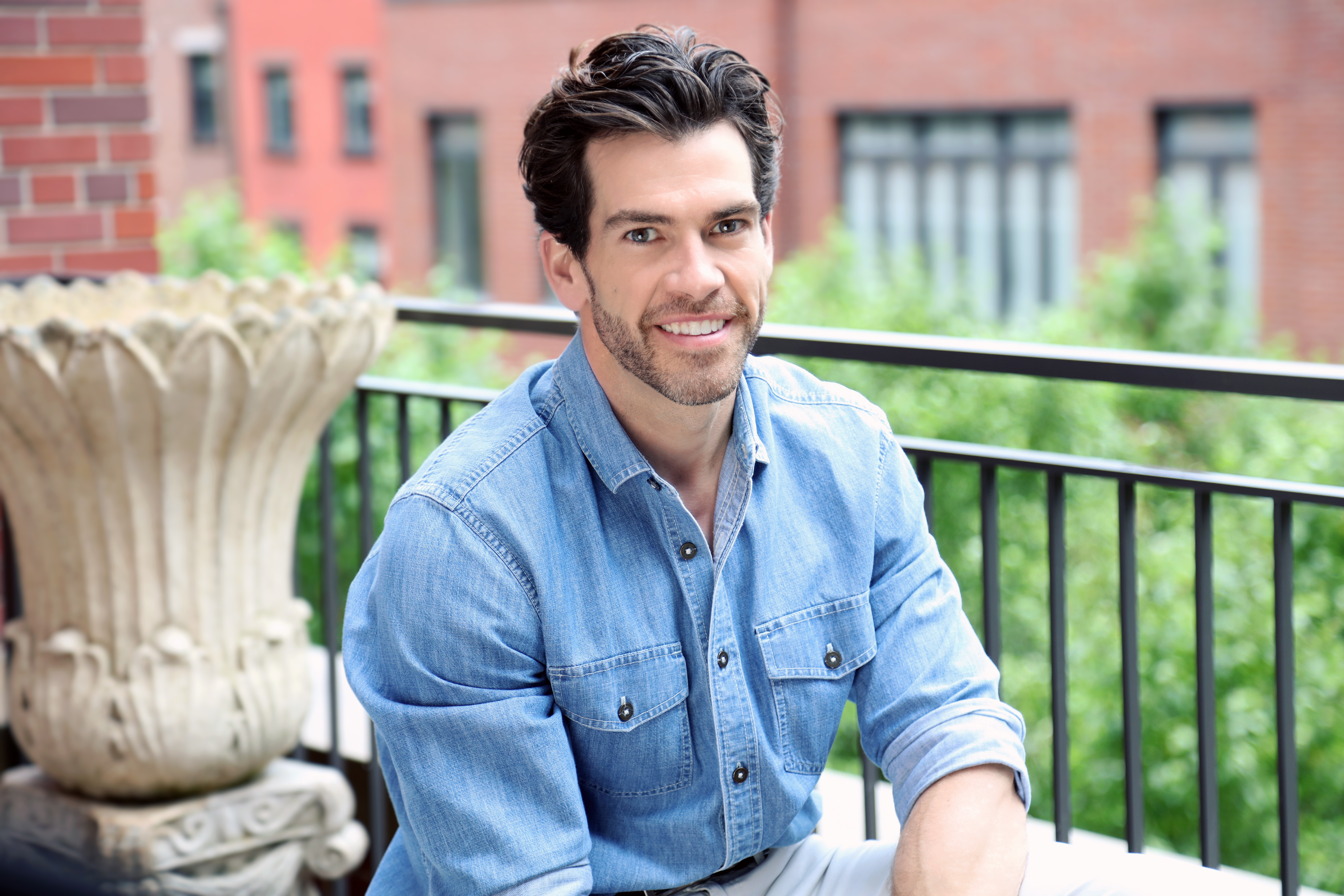 A man in an open-collar shirt on a terrace, smiling into the camera.