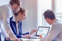 3 people looking at a computer in an office.