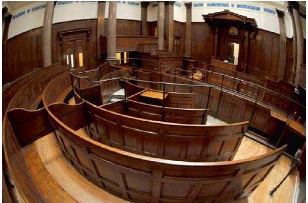 Fig. 18: Old courtroom. http://www.istockphoto.com/stock-photo- 6656352-inside-st-george-s-hall-in-liverpool.php. © iStockphoto  7 This is, of course, just an impression. I came across reports on, for instance, the new Crown Court in Manchester that apparently did not fulfil its functions. The build- ing, it was claimed by those working in it, “does not work.’ The staff criticized the slow security checks, the lack of conference rooms and storage space for files, the tiny library, and the uncomfortable barrister’s lounge. See The Guardian, 30th June 2004.  SLIV CUUIEL MEMES SEOUL S A LUO UL BAMIIEALA SS A Lidooitdl Ulitalir,.  The other court looked entirely different. It is hosted in a functional building from the 1980s. The entrance area reminds of an airport. Scores of people pass quickly. Trials are announced on screens like flight arriv- als/departures. Inside the court, the atmosphere is business-like. White walls, light furniture, no decoration - the rooms evoke efficacy rather than greatness. Plain carpets swallow most of the noise made by shoe heels and file trolleys. Moving through these courtrooms - entering. crossing, and leaving them - seems less distracting. The court resembles a machine emitting cases and judgements. 