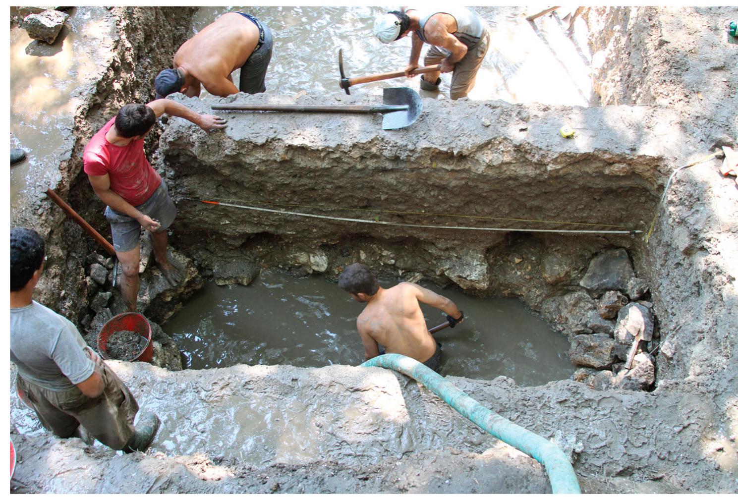 Figure 9. Excavation of the drainage trench in Unit 21 in 2012, showing the narrow baulk partitioning the wet trench and the shoring of the drainage trench wi stones.  “It was found that more than half of the cultural deposits in the lower city are waterlogged, representing material culture dating from the origins of the city in the second half of the  7th century B.c. up through to the High Roman Empire (FIGURE 10). Problems with dewatering became the limiting  A continuously stepped trench to such depths (greater than 4 m), as required in the lower city of Butrint, presents hazards. To ensure trench stability and avoid collapse, it was imperative to design the wet trench to be much smaller than the main trench and to place it some distance away from the walls of the main trench, so that the wet trench effec- tively served as a separate trench altogether and did not form part of a continuously stepped trench from the surface. Thus, the size of the initial (main) trench had to be very large in the  ower city of Butrint to permit wet-site excavation. The RFE Project followed the guidelines established by OSHA, the  