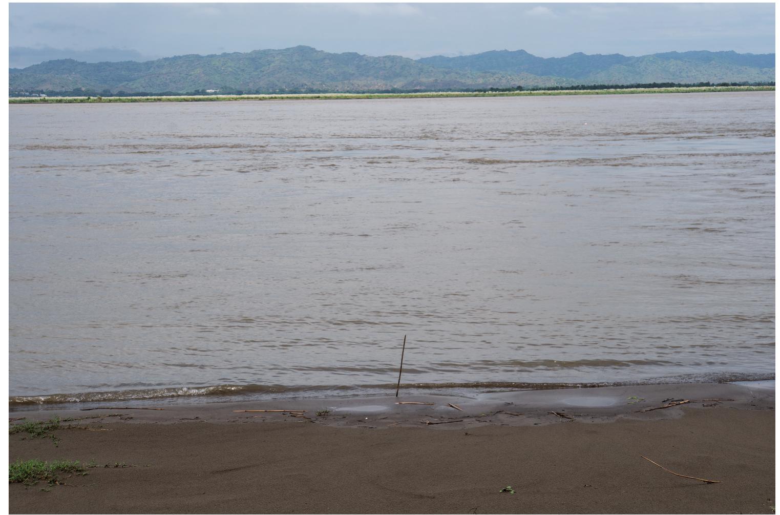 FIGURE 2 Saltating sediments held in suspension in the Ayeyarwaddy River, Bagan, Myanmar, September 2019. Photograph by the author.  knowing what will happen next (see Figure 2). They move in their transportation medium by saltation (McGee 1908). This is not a commonly used word. It comes from the Latin salire, to leap and saltare, to dance. It describes how, whether dragged along a surface or held in suspension in turbulent eddies of air or water, sediment particles bounce, jump, leap, roll or tumble along (Parsons, Cooper, and Wainwright 2015). They become terra-aqueous particles of matter, barely distinguishable from the dynamics and characteristics of the fluids that carry them. Geologists describe what transpires when sediments saltate as a complex interplay between particle substance and size, fluid velocity, gravity, slope, channel width and depth, bed surface and so on (Gilbert 1914). The physics of these processes is chaotic and emergent (Church 1996). At low fluid velocities, sediment particles roll downstream, staying in contact with the bed-surface. Here the forces exerted by the fluid on the particle are only enough to roll it along. As the fluid velocity increases, its drag and lift forces may become sufficient to lift sediment particles against gravity from the surface, in a trajectory “analogous to that of a cannon ball” (Gilbert 1914, 28). Particles are accelerated by the fluid, but pulled downward by gravity at the same time, causing them to travel in roughly ballistic trajectories (Gilbert 1914; Kok et al. 2012). Ifa particle has been sufficiently accelerated by a fluid, it may bounce up again and eject or splash other particles in saltation, which propagates the process further (Bagnold 1941). A particle might also disintegrate on impact or eject much finer sediment from its surface. In air, this process is known as saltation bombardment, and creates most of the sand in sand storms (Shao 2008). Sediments are thus not only transported by saltating, they are  