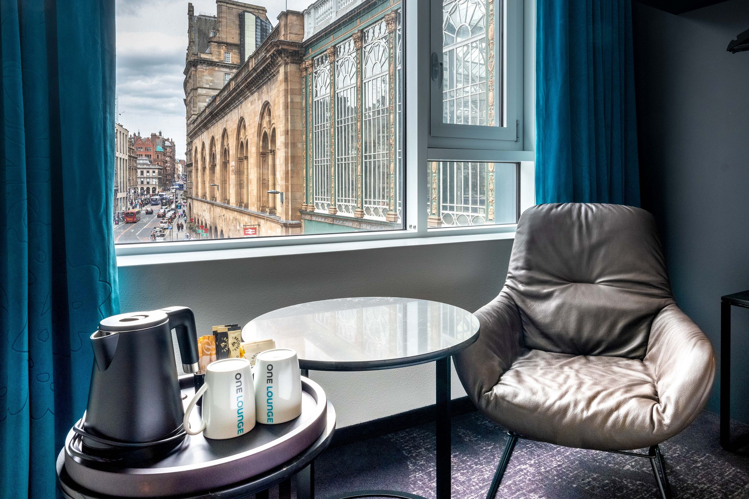 hotel Glasgow Motel One room with armchair, side table, electric kettle, and two cups in front of a large window