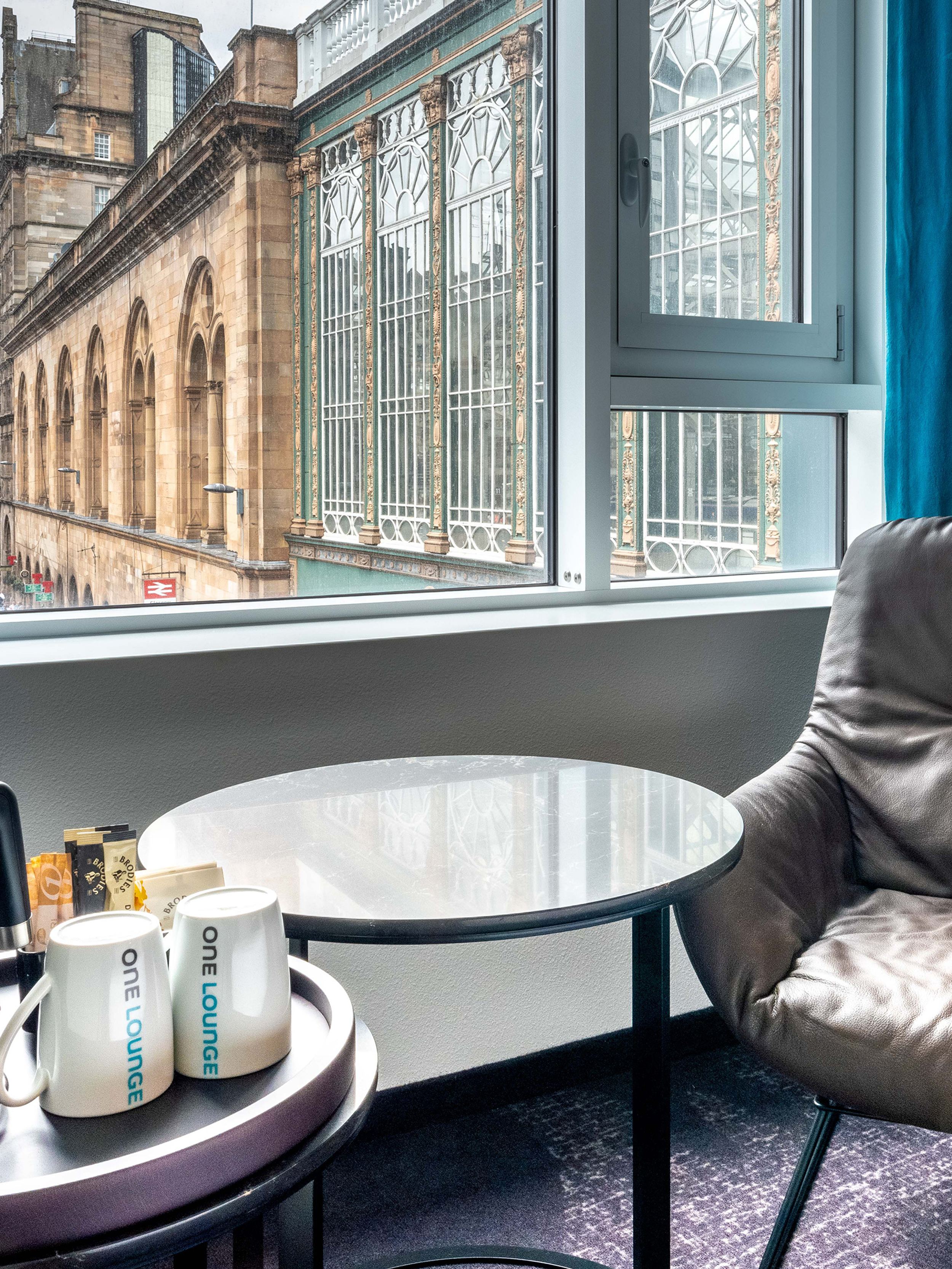 hotel Glasgow Motel One room with armchair, side table, electric kettle, and two cups in front of a large window