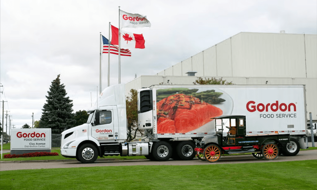A white Gordon Food Service semi-truck parked in front of a distribution center