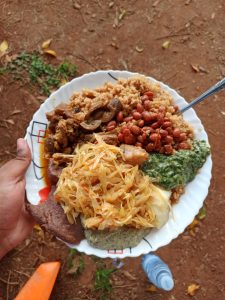 A plate packed with a variety of local foods, including pilau rice, beans, beef stew, and steamed cabbage. \