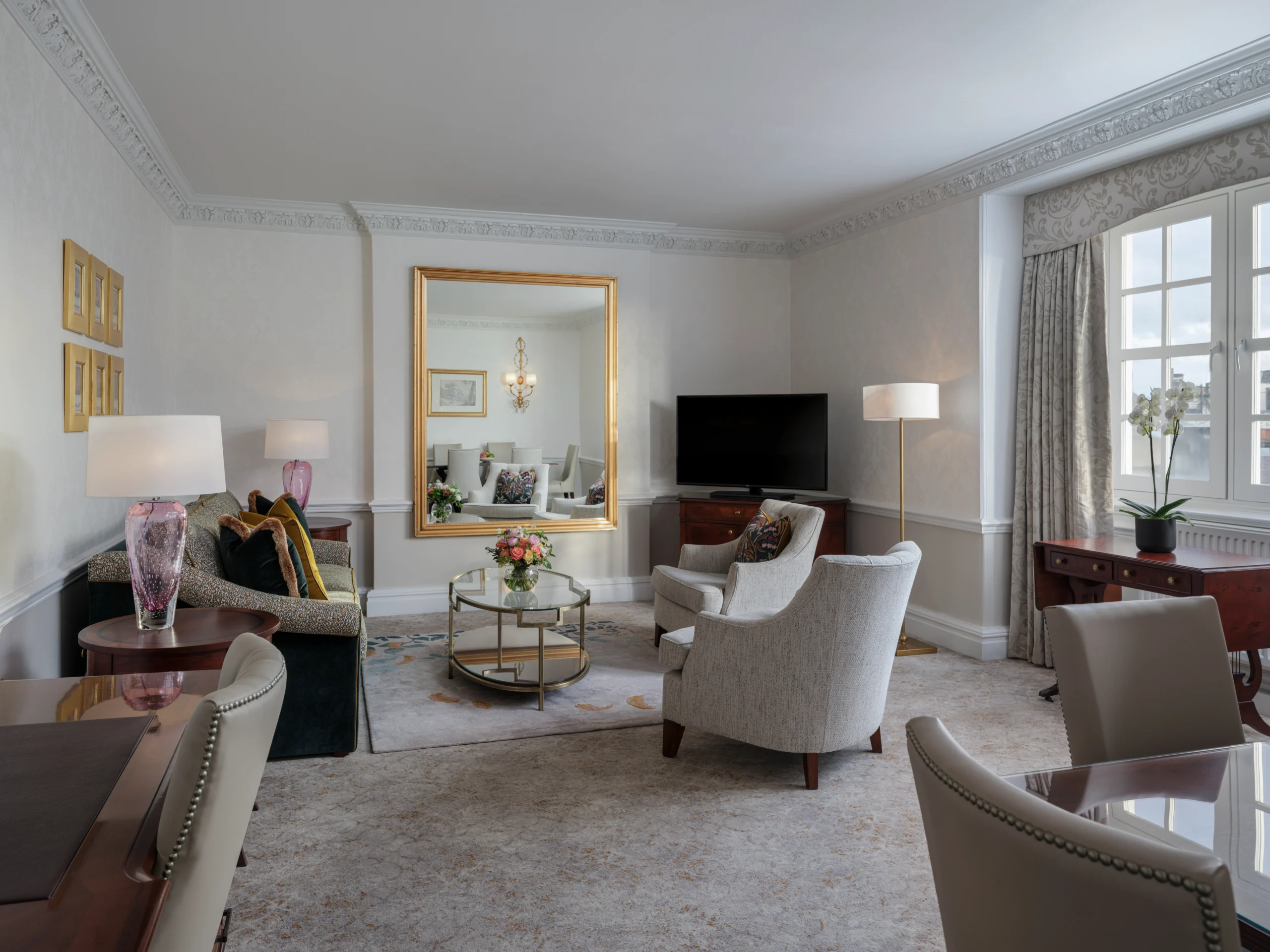 Large living room with plush sofas, area rug and coffee table, dining table, armchairs, window treatments and art on walls