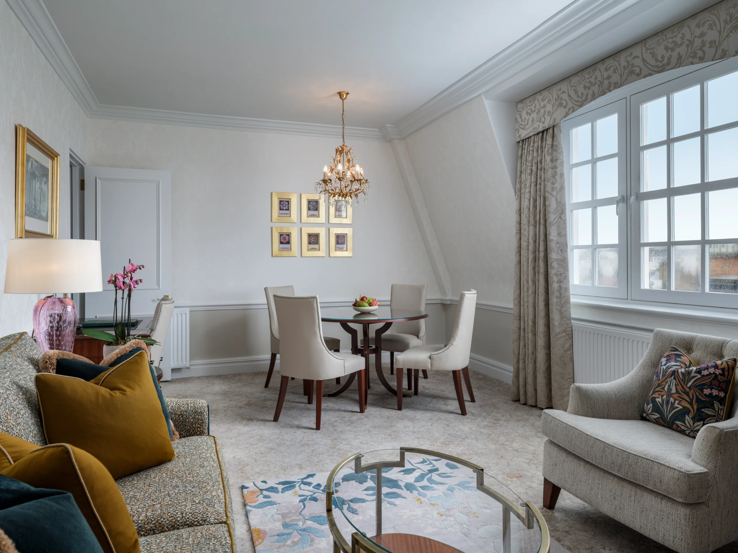 Large living room with grey sofas, coffee table, dining table, armchairs, window treatments and art on walls