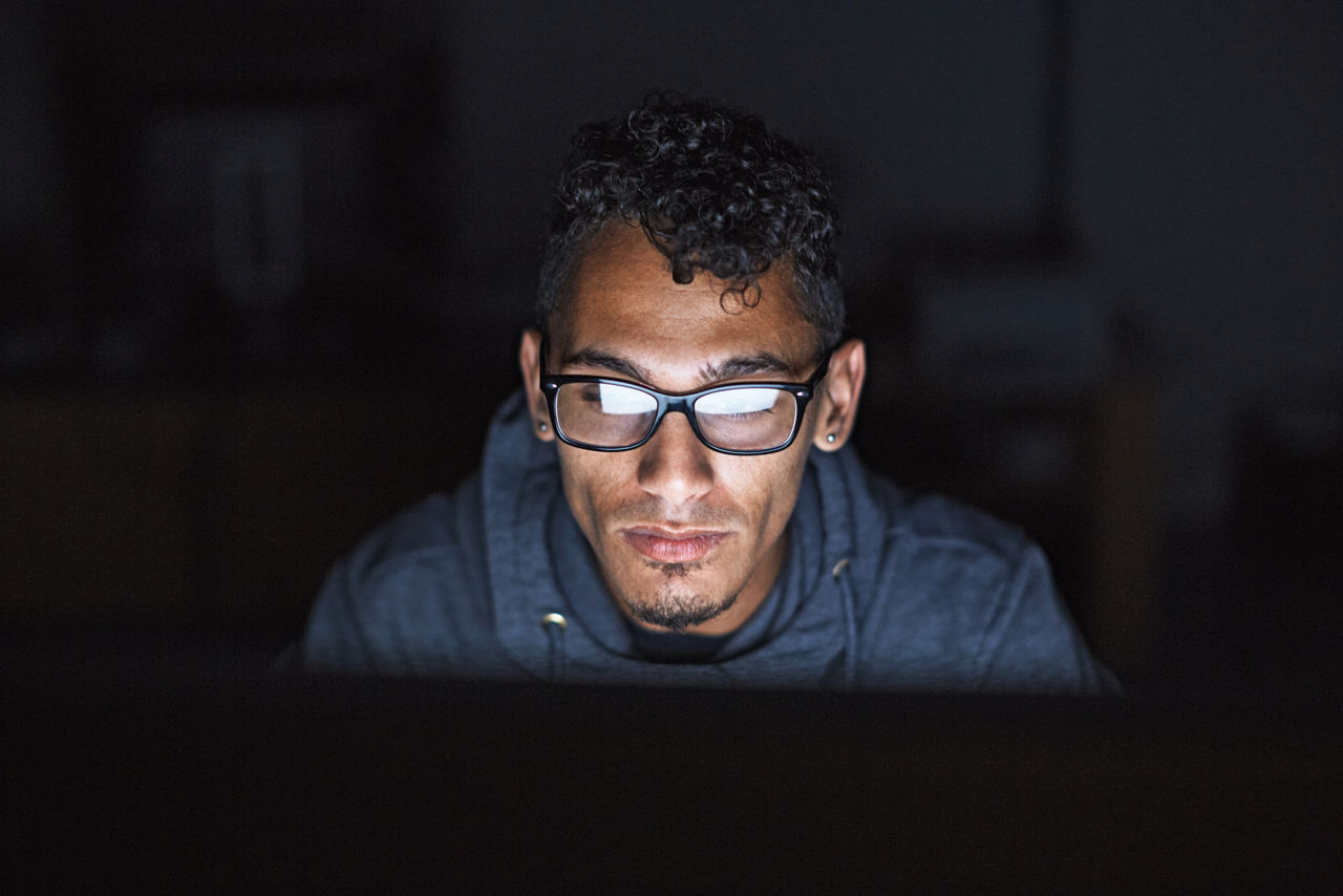 man wearing glasses working in the night at a desktop computer.