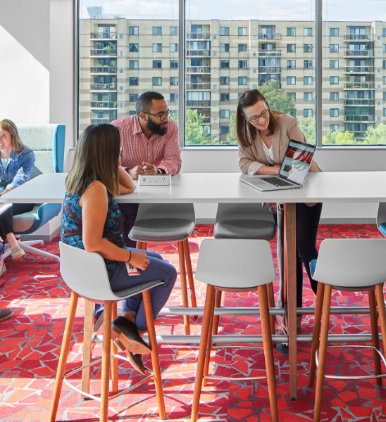 three associates at a meeting table looking at a laptop