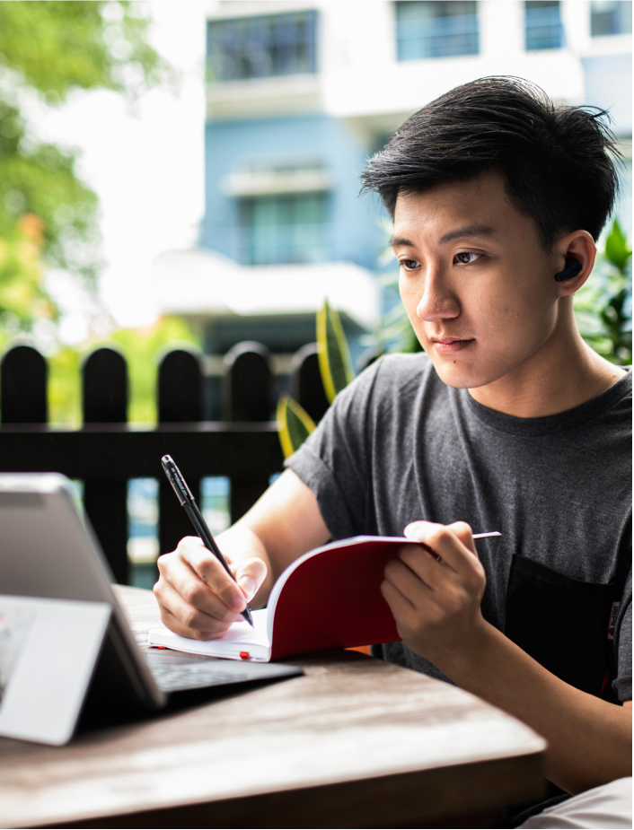Image of someone writing in their notebook while the watch something on their tablet