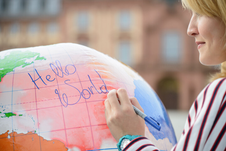 Internationale Studierende Eine Frau schreibt "Hello World" auf eine große aufgeblasene Weltkugel.