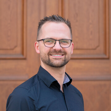 Lukas Dausend hat kurze braune Haare und einen Bart. Er trägt eine Brille und ein schwarzes Hemd.